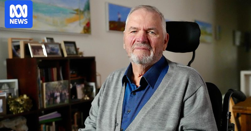 A man wearing a collared shirt and cardigan sits in a house. He looks into camera with a serious expression.