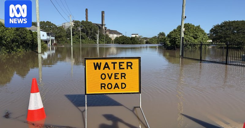 A yellow 'water over road sign' infront of a flooded road.