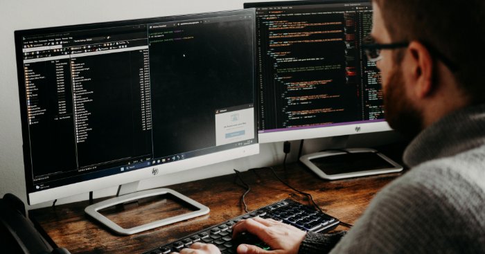 A man types while looking at two computer monitors.