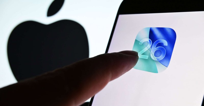 Dedo de pessoa quase tocando ícone do iOS 26 em tela de celular colocado na frente de tela maior exibindo o logotipo da Apple