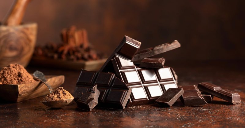 Bar of dark chocolate bar, with cocoa powder on a brown table.