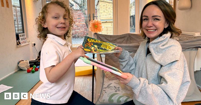 Romi, who has blond curly hair and is wearning a white t-shirt, is passing a book to his mum, Alexis who has short brown hair and is wearning a grey hoodie. She is passing a digital device with a colourful cover back to him and both are smiling.