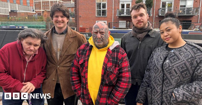 Four men and a woman in coats standing in a row in front of some large buildings