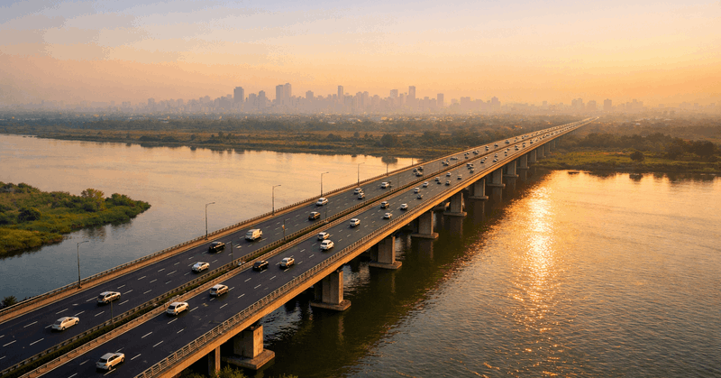 Aerial view of a multi-lane elevated bridge crossing the Yamuna River connecting Noida to Delhi with city skyline visible in the background at golden hour, 2026