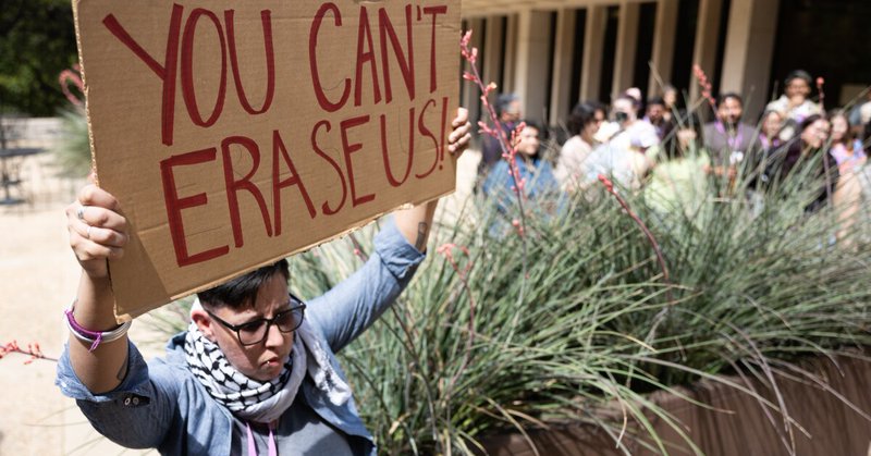 A person holding a sign that reads "You can't erase us"