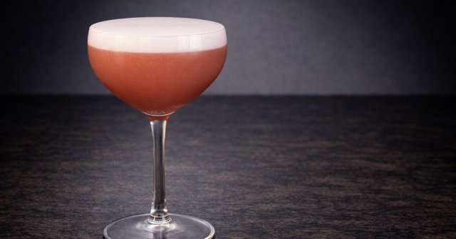 A pale yellow cocktail in a tumbler garnished with a lemon wheel and a salt rim.