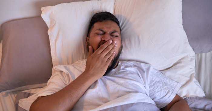 Un hombre bosteza mientras intenta dormir