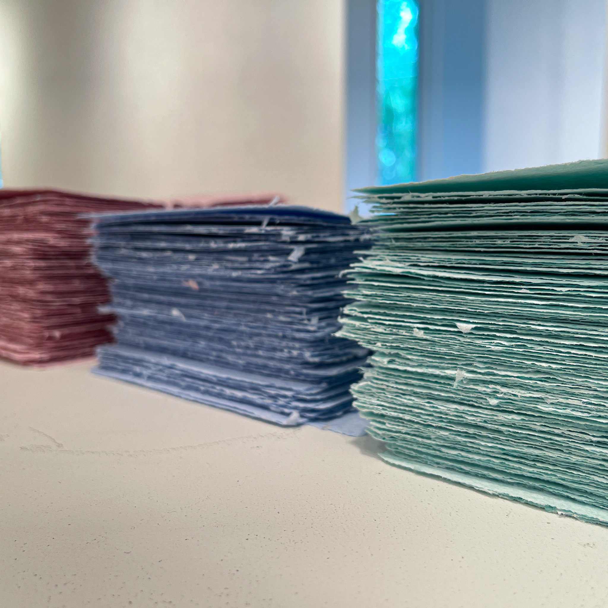 Side shot of 3 stacks of scrubs paper. There is a green stack, blue stack, and pink stack.