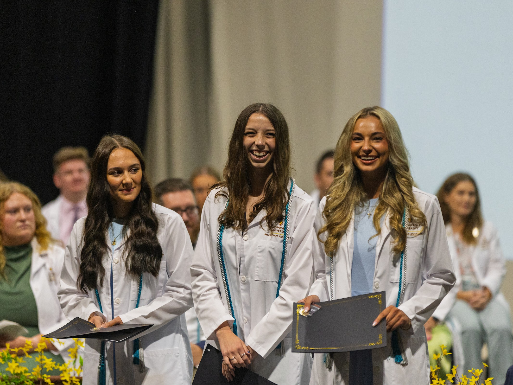 Three Valparaiso University master of science in physician assistant studies students smile during their white coat ceremony.