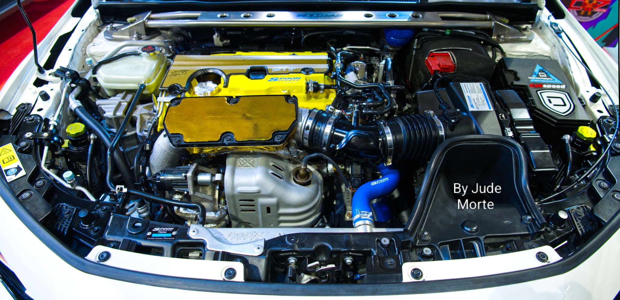 2021-present Honda Civic engine bay, taken with the camera 📷 looking down at the mechanical + electronic array of assembled car parts.
The yellow and blue parts on this Civic engine bay were from Spoon Sports.
Spoon Sports is a purely Japanese domestic market (JDM)-Honda cars auto aftermarket parts peddler.
This postcard is from the 13-16 November 2025 Manila Auto Salon (MAS), SMX Convention Center-SM Mall of Asia, Pasay City, Philippines 🇵🇭 
The annual MAS is the 🇵🇭 equivalent of the once-a-year Specialty Equipment Market Association (SEMA) custom car-auto aftermarket products show in Las Vegas, Nevada, USA 🇺🇸