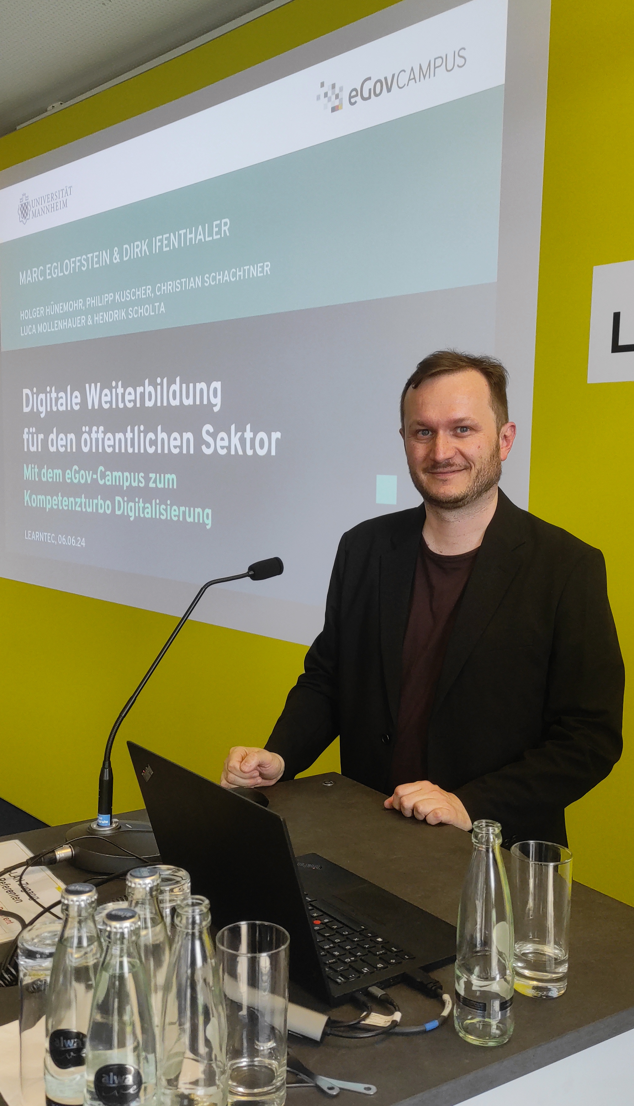 Foto von Marc Egloffstein am Moderationspult. Im Hintergrund die Präsentationsfolien.