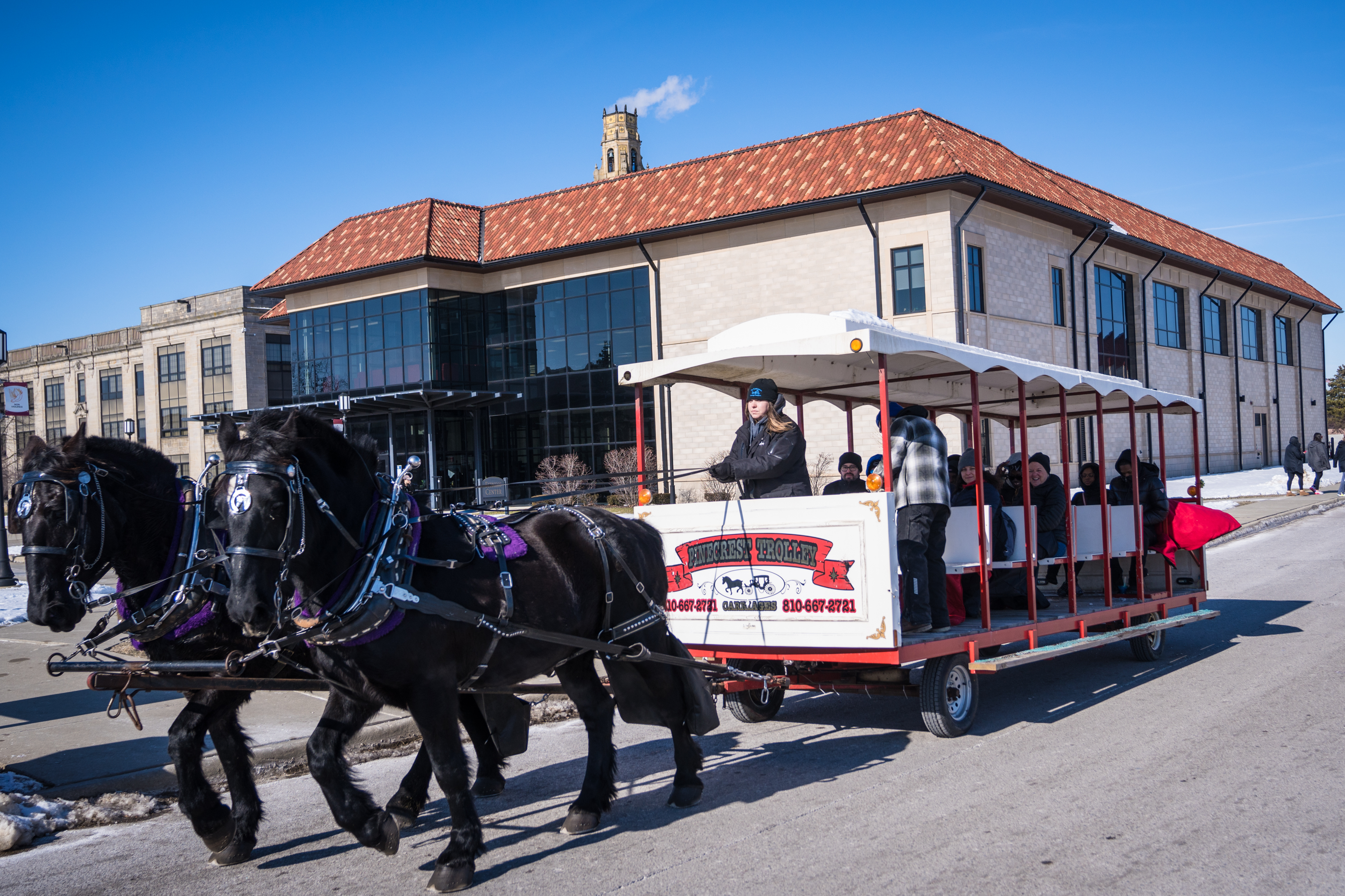 A horse-drawn trolley gives rides to more than a dozen people outdoors in front of the Student Fitness Center.
