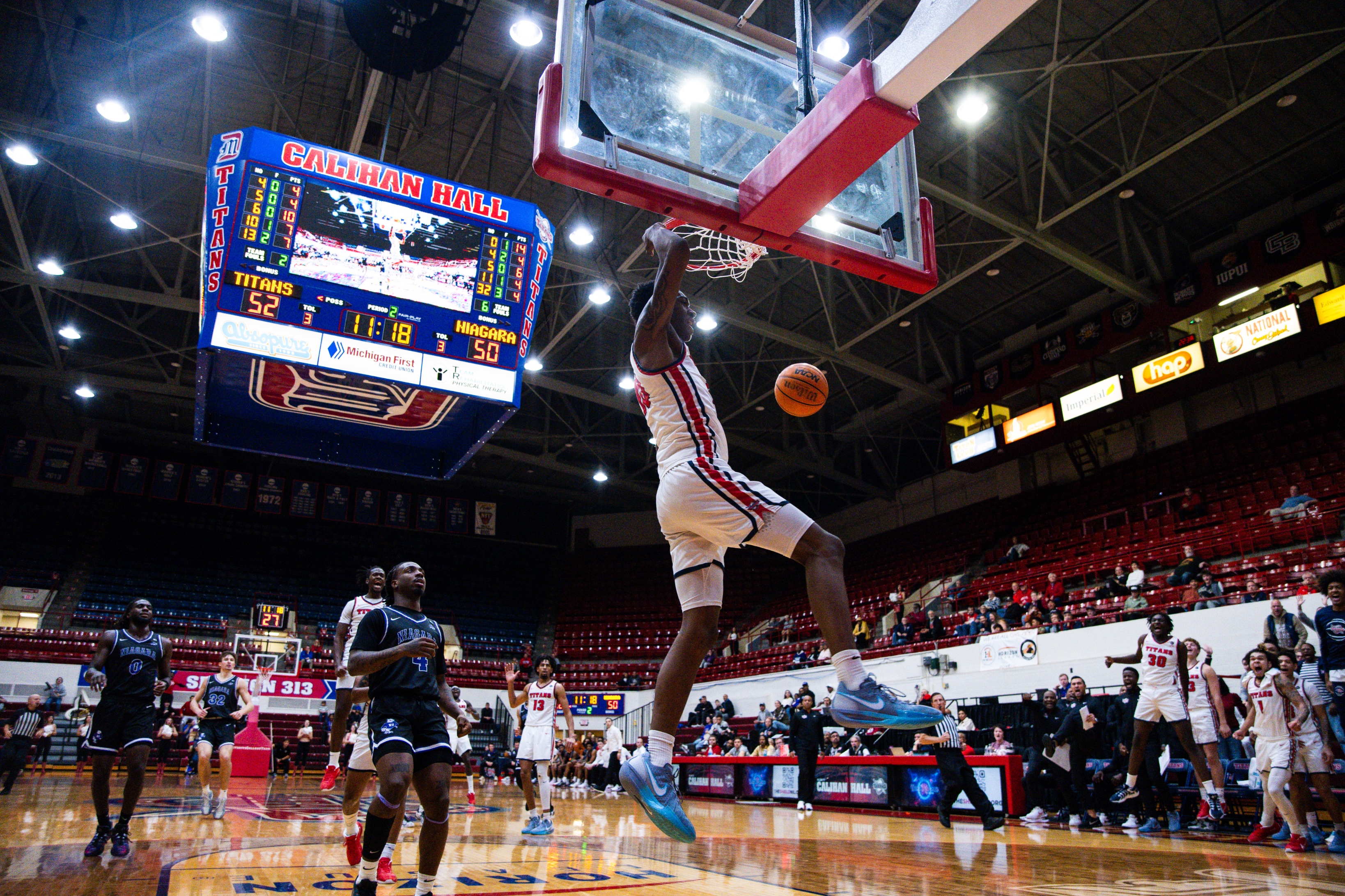 A Titan basketball player dunks the basketball during a home game inside of Calihan Hall, with many others looking on.