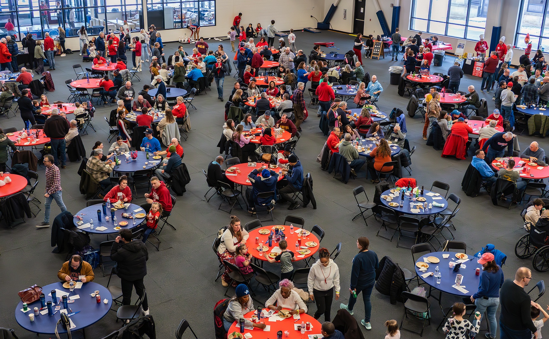 People sit and mingle at red and blue tables inside of the Student Fitness Center during the Titan Winter Blast.
