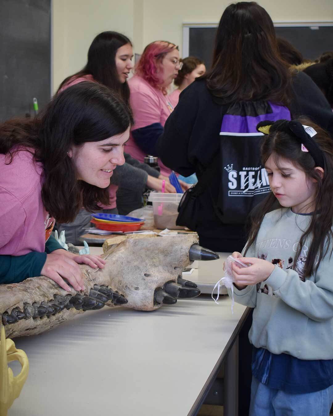 A woman in a pink t-shirt shows off a large toothed fossil of a young girl.