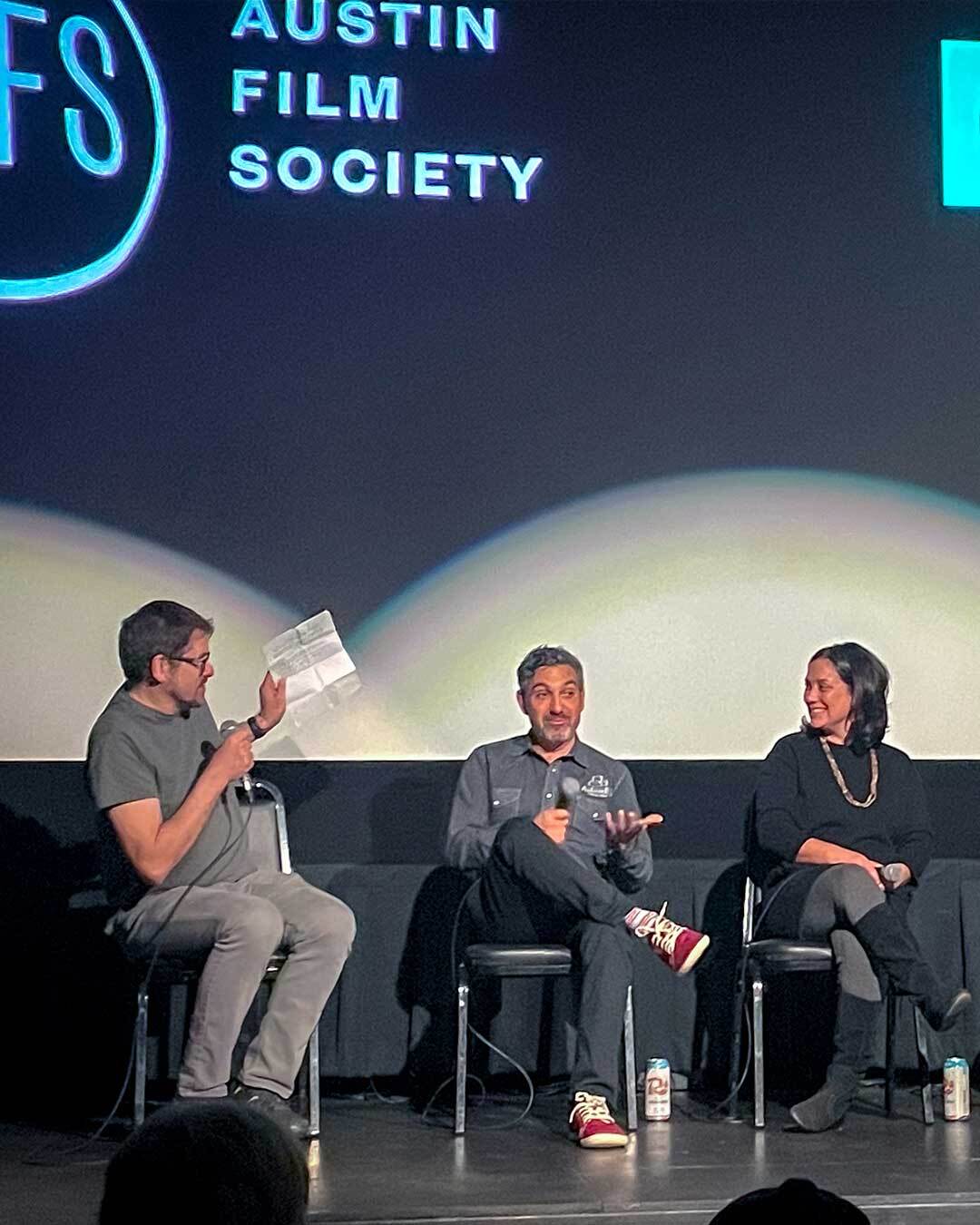 Three people sit on a stage having an animated discussion beneath a sign reading “Austin Film Society.”