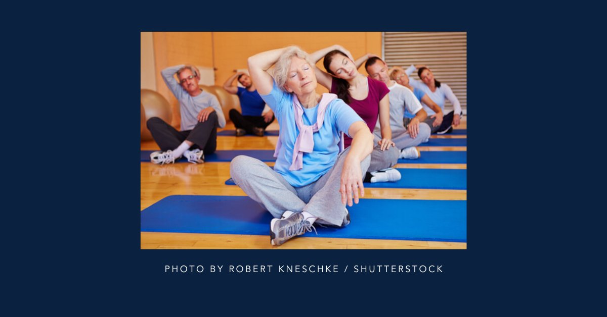 A group of people on yoga mats and stretching with their right arm over their head and leaning to the side.