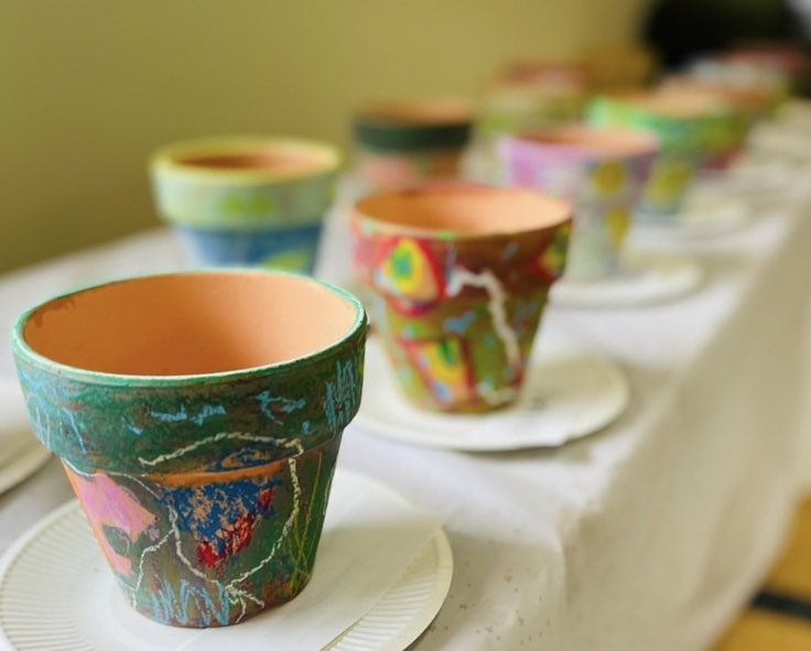 植木鉢にオイルパステルで種や根っこをイメージした絵が描かれています。鑑賞会のために作品が並べられています。