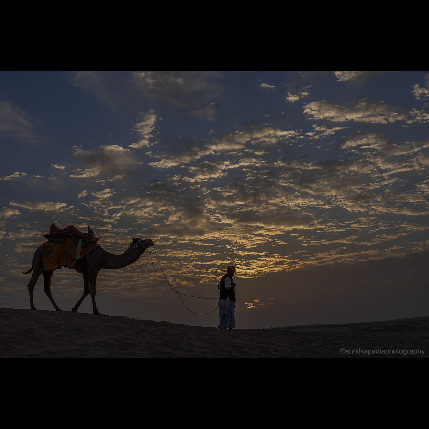 A color image of a landscape in the form of a sunrise with dramatic clouds in a desert named as Khuri. The man and the camel are on their way to begin their errand for the day. Jaisalmaer, Rajasthan, India
I shot this image to depict the dramatic sunrise with serenity and tranquility at the desert of Khuri, Jaisalmer, Rajasthan, India
All my images in color and/or black-and-white are very artistic, elegant and heart-warming. They shall be a proud possession as wall art for your houses and offices.
For more choices of Photo Art Prints, please visit:
www.photo4me.com/profile/sunilkapadiaphotography