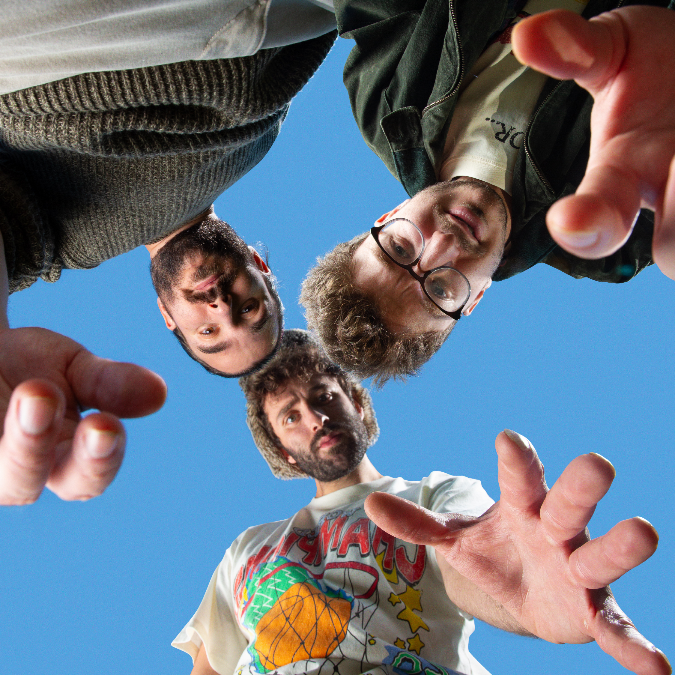 Three memebers of the Band AJR looking down into the camera with a blue sky in the background. It looks like all three are reaching down to pick up the camera that's taking the photo.