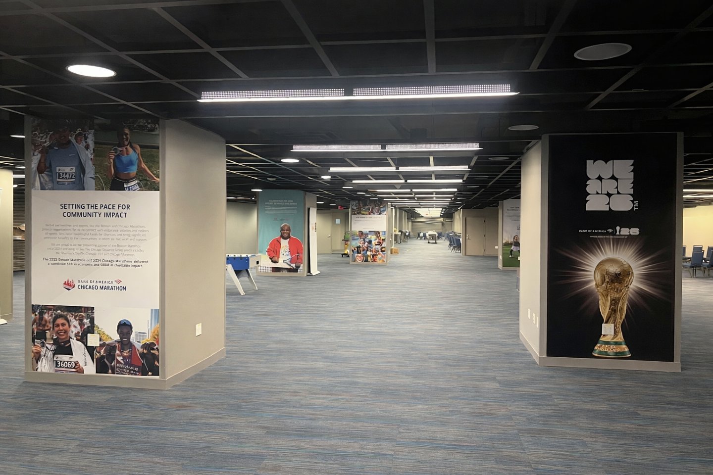 Spacious indoor hall with blue carpeted floor, pillars wrapped in posters including Chicago Marathon and a golden trophy.