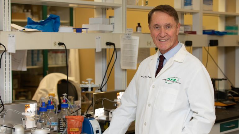 man posing in a medical lab wearing a white lab coat.