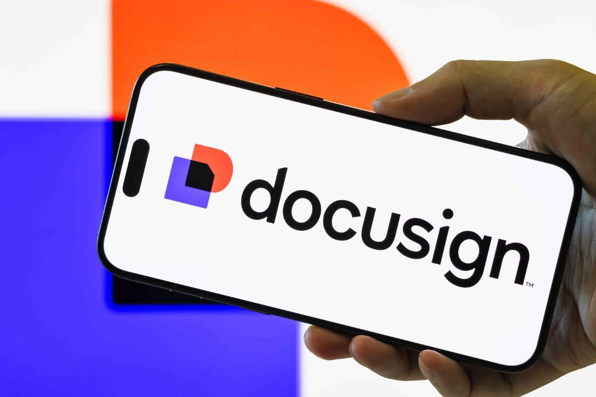 A hand holding a smartphone displaying the DocuSign logo, reporting strong revenue and earnings growth.
