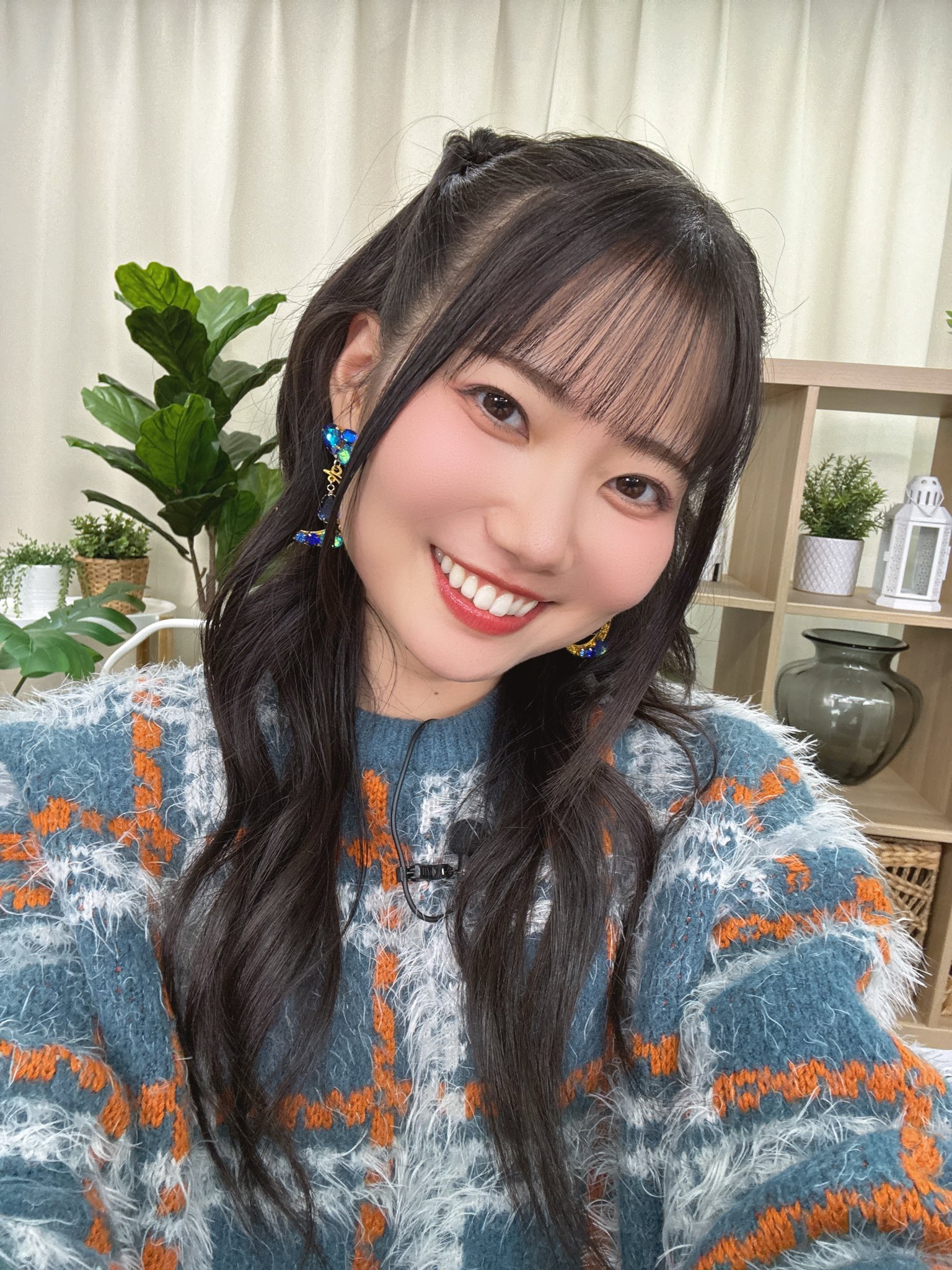 笑顔のおじかなおの自撮り写真。
髪型はハーフツインで、青色に白とオレンジのチェック柄のセーターを着ている。