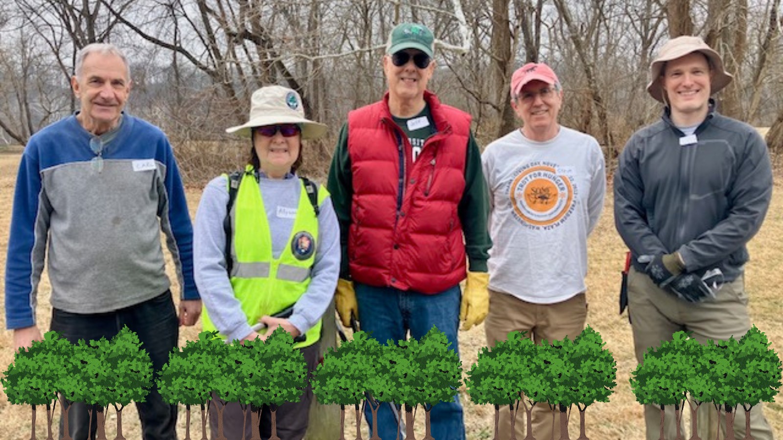 Group of five people standing outdoors in casual and safety gear, surrounded by leafless trees in a natural setting.