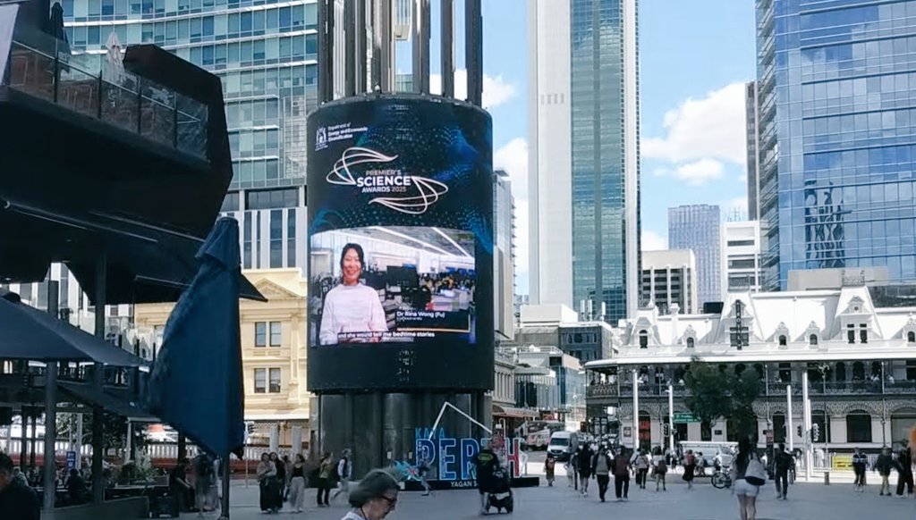 Giant digital cylinder light display with Premier's Science Award 2025 winner scientist Dr Rina Wong (Fu), amongst tall high rise buildings 