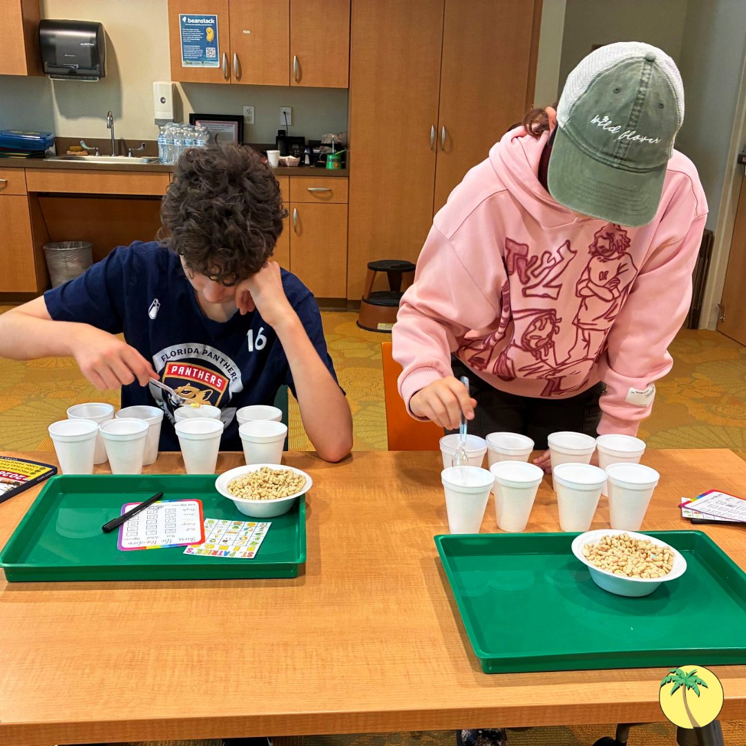 Two teenagers picking apart a bowl of Lucky Charms cereal and sorting the pieces into styrofoam cups. They have tally cards to measure how many of which charms they have.