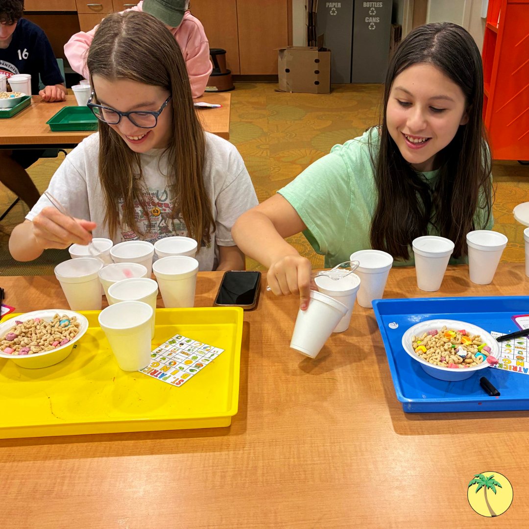Two teenagers picking apart a bowl of Lucky Charms cereal and sorting the pieces into styrofoam cups. They have tally cards to measure how many of which charms they have.