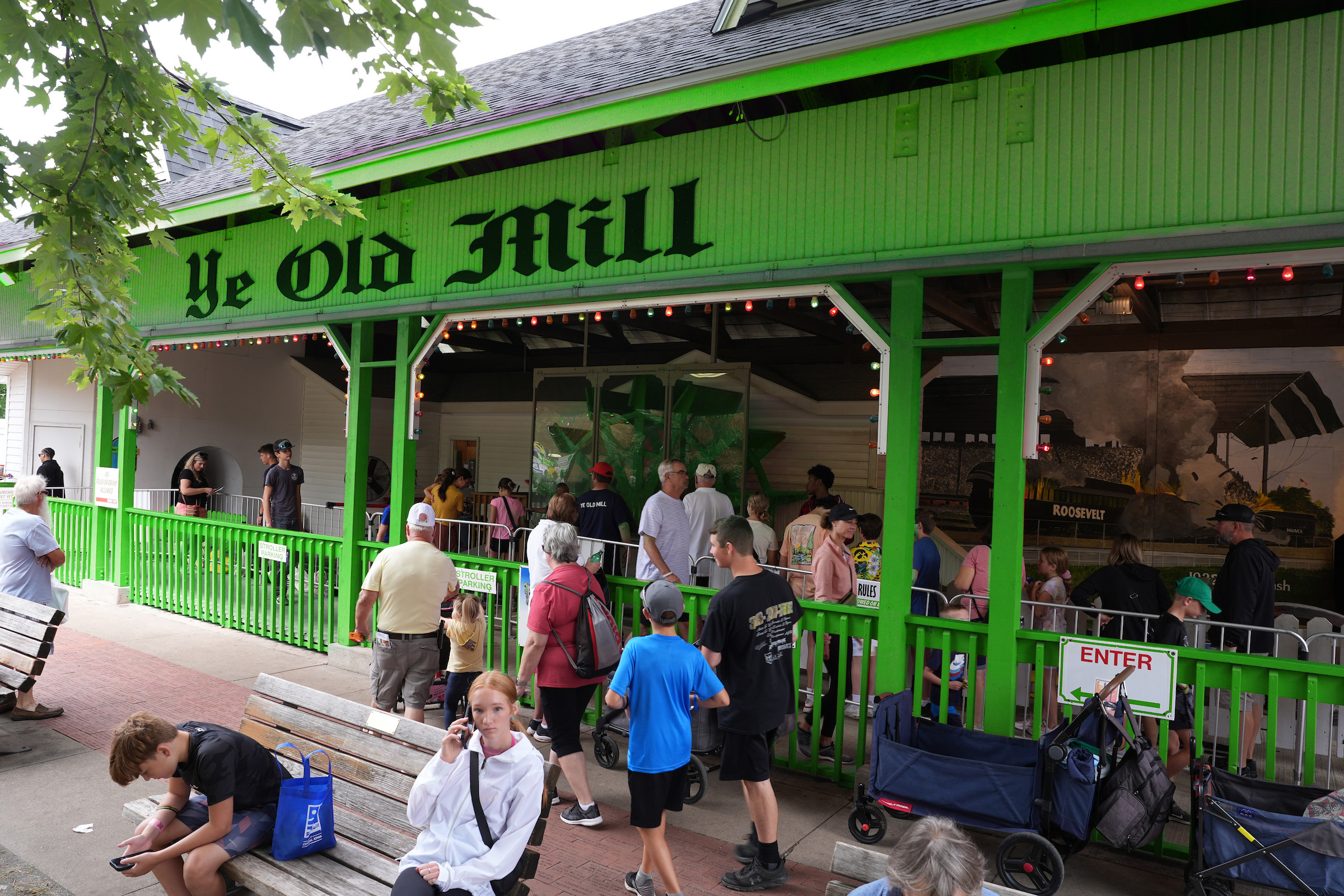 The Ye Old Mill at the Iowa State Fair but recolored to look green instead of red. A group of people are seen walking around and waiting in line to ride the attraction. 
