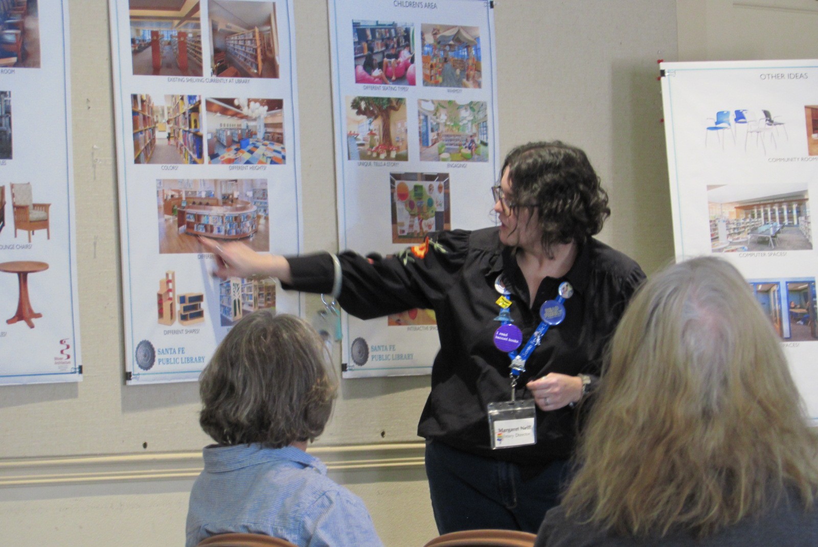 The library director points at photos on the wall representing different types of library furniture.