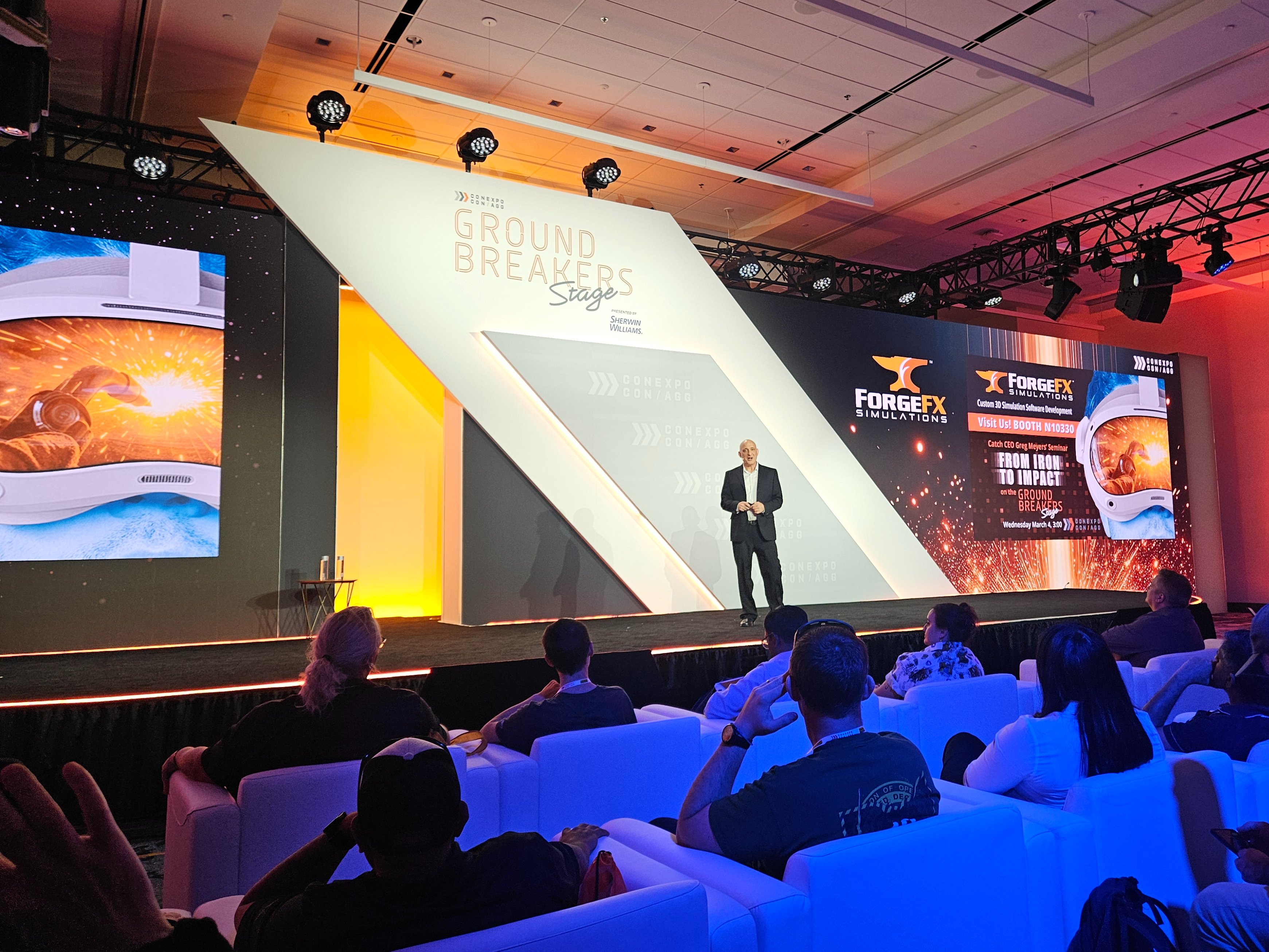 ForgeFX Simulations at CONEXPO-CON/AGG 2026: team members pose at the booth in front of a large video wall; CEO & Co-Founder Greg Meyers presents “From Iron to Impact” on the Ground Breakers Stage; attendees watch the session from white lounge seating; and visitors test immersive heavy equipment training demos using VR headsets and a bright orange lift simulator. Additional images show hands-on operator training, booth conversations, and live demonstrations of spatial computing-based training developed with partners including PICO XR. The photo set captures ForgeFX’s post-show highlights, customer engagement, and the company’s focus on safer, faster, and more measurable training for construction and industrial equipment operators.