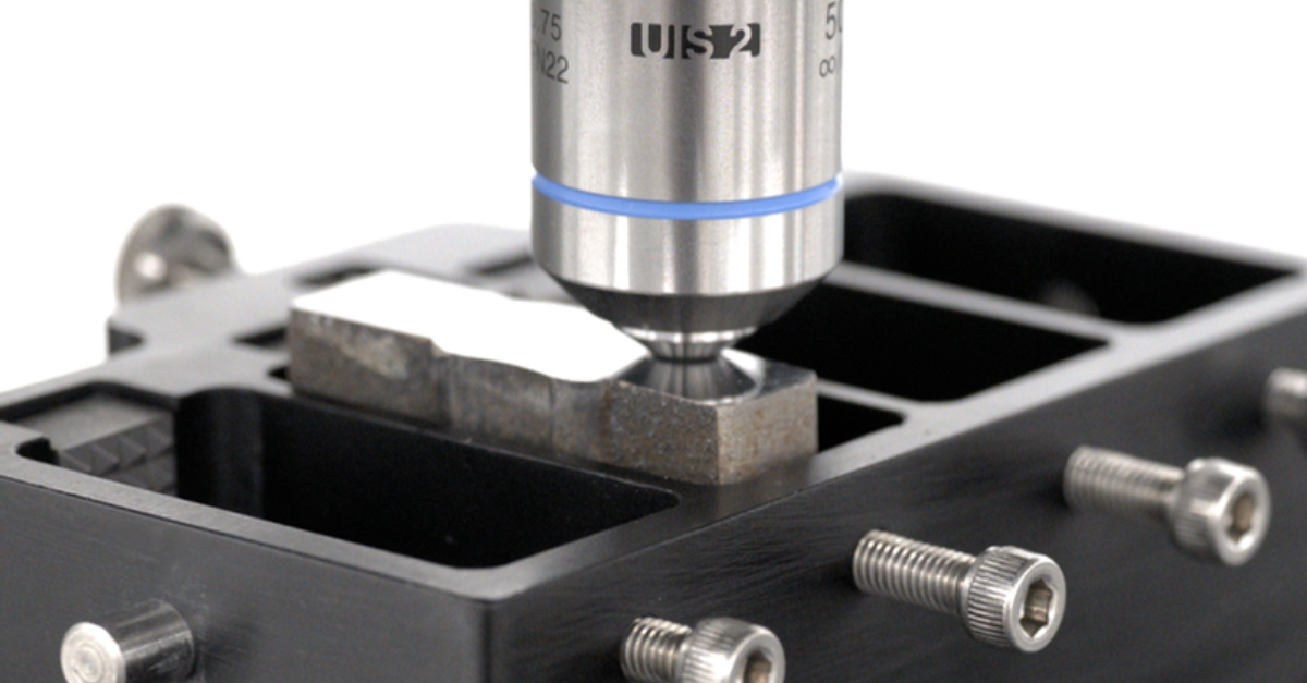 Close-up of a precision measuring instrument inspecting a metal component on a black fixture with screws.