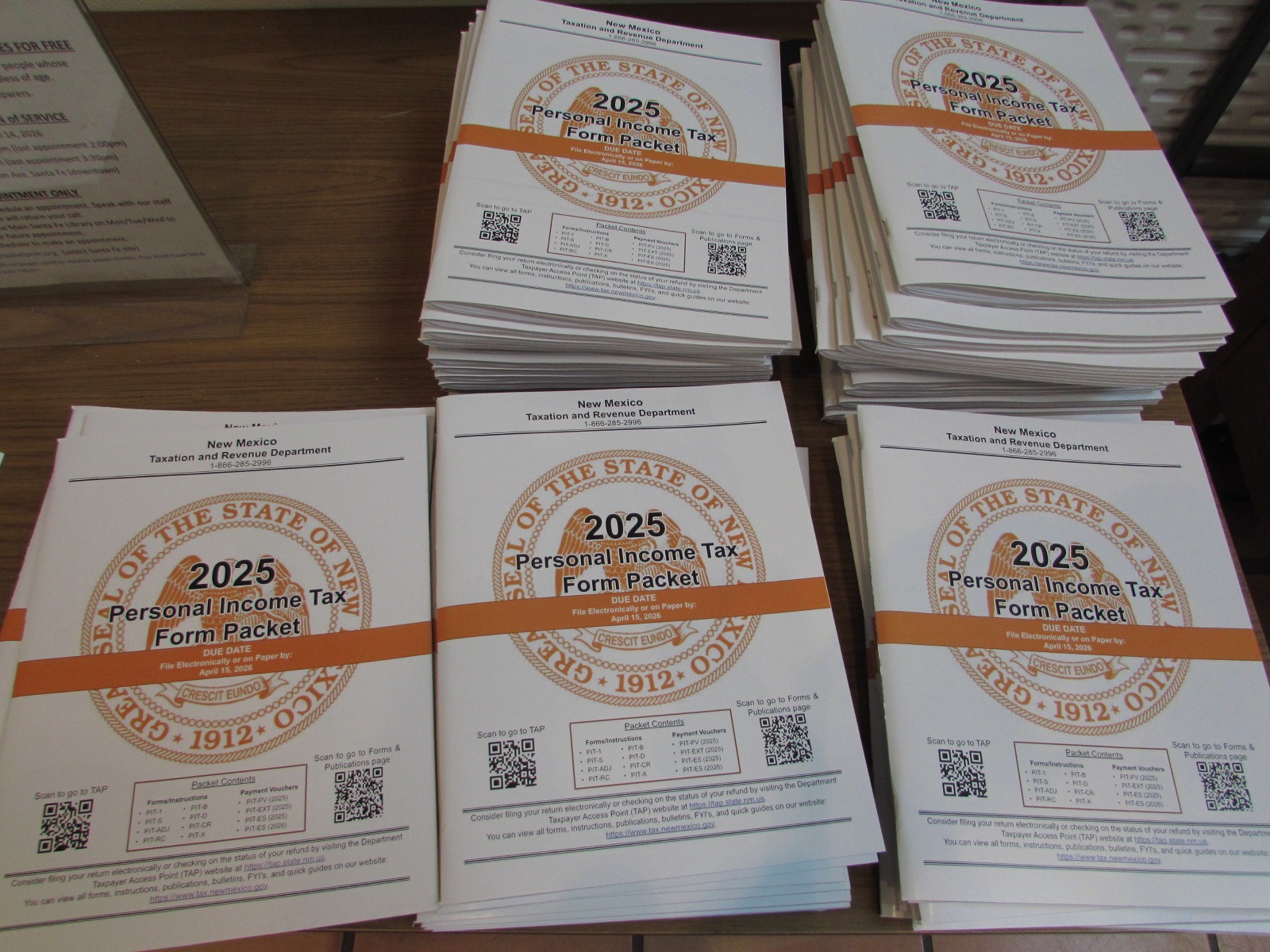 Five piles of 2025 New Mexico PIT Form tax packets on a wooden table.