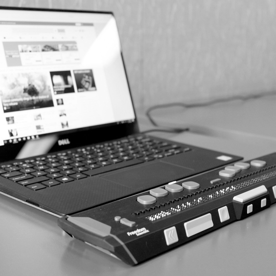 a laptop computer sitting on top of a desk with a refreshable braille display.