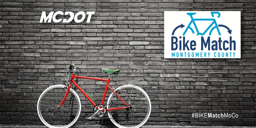 Red bicycle with white wheels parked against a dark brick wall featuring the MCDOT logo and Bike Match Montgomery County sign.