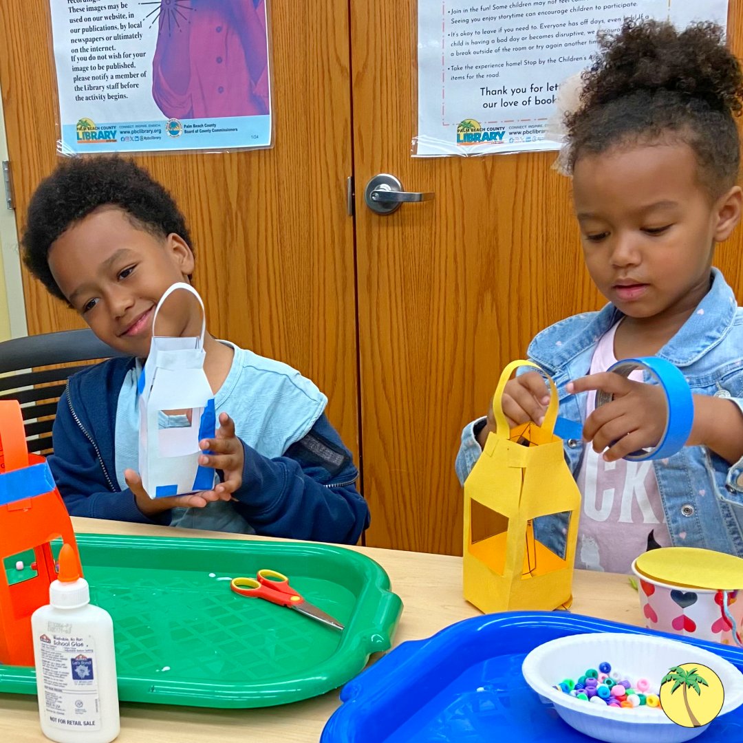 Two elementary-aged children crafting paper lanterns, surrounded by tape, glue and beads.