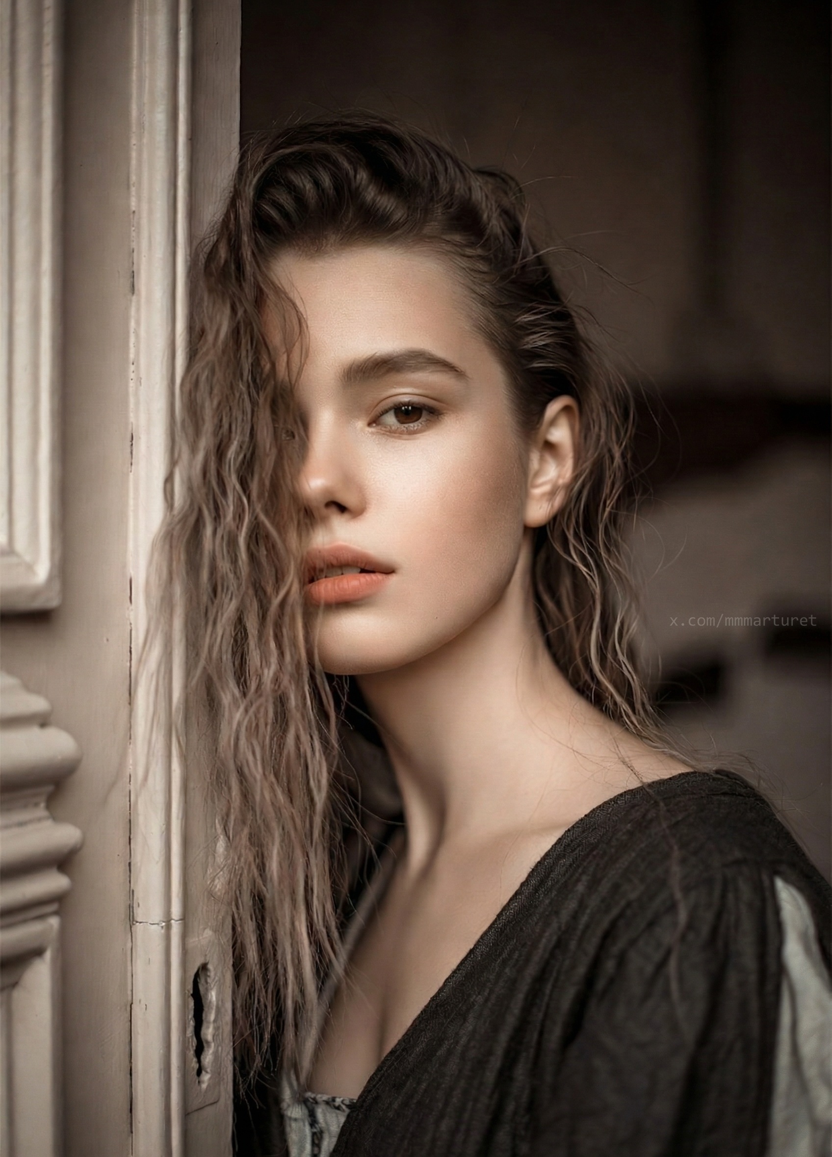 Retrato de una mujer joven con cabello húmedo cayendo sobre su rostro, apoyada en una puerta antigua de madera, con luz suave y tonos cálidos que crean una atmósfera íntima y nostálgica.