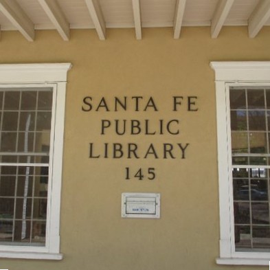 Front of Main Library building; two large windows and the words SANTA FE PUBLIC LIBRARY 145 on the adobe wall in the middle of them.