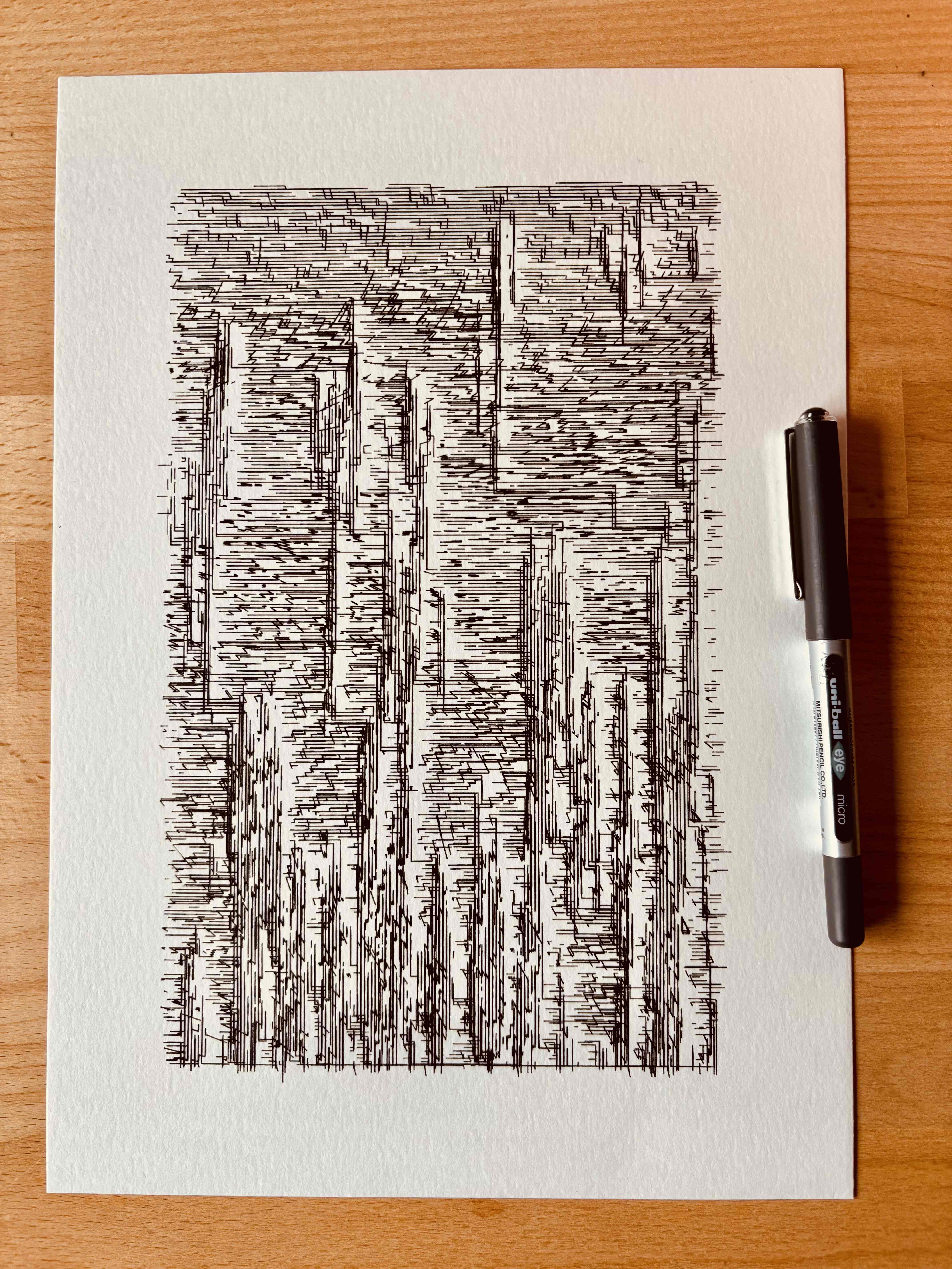 Black ink abstract drawing of vertical lines and patterns on white paper, with a pen placed beside it on a wooden surface