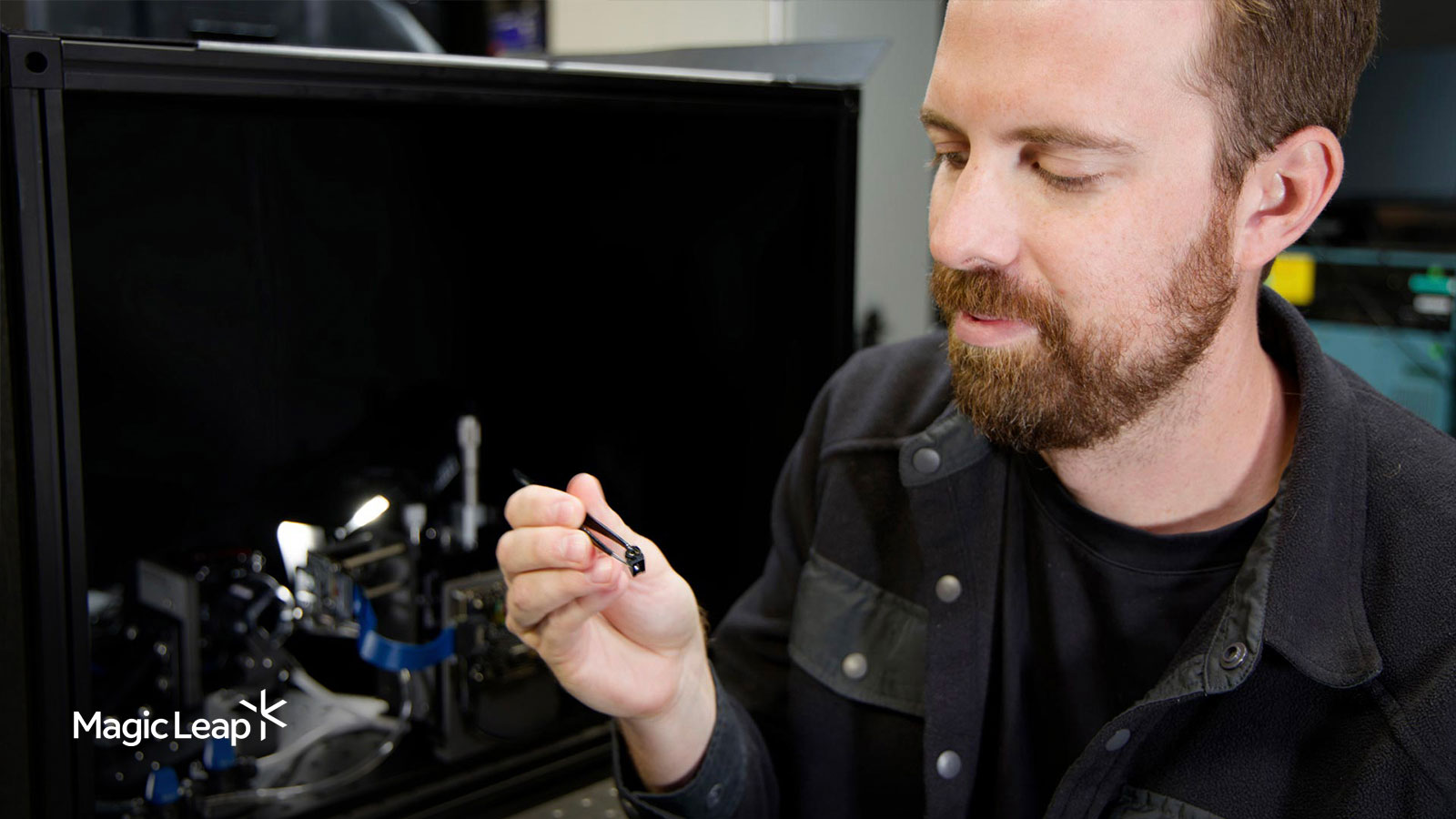 A Magic Leap engineer holds a light engine projection lens with tweezers near a proprietary quality control measurement tool.
