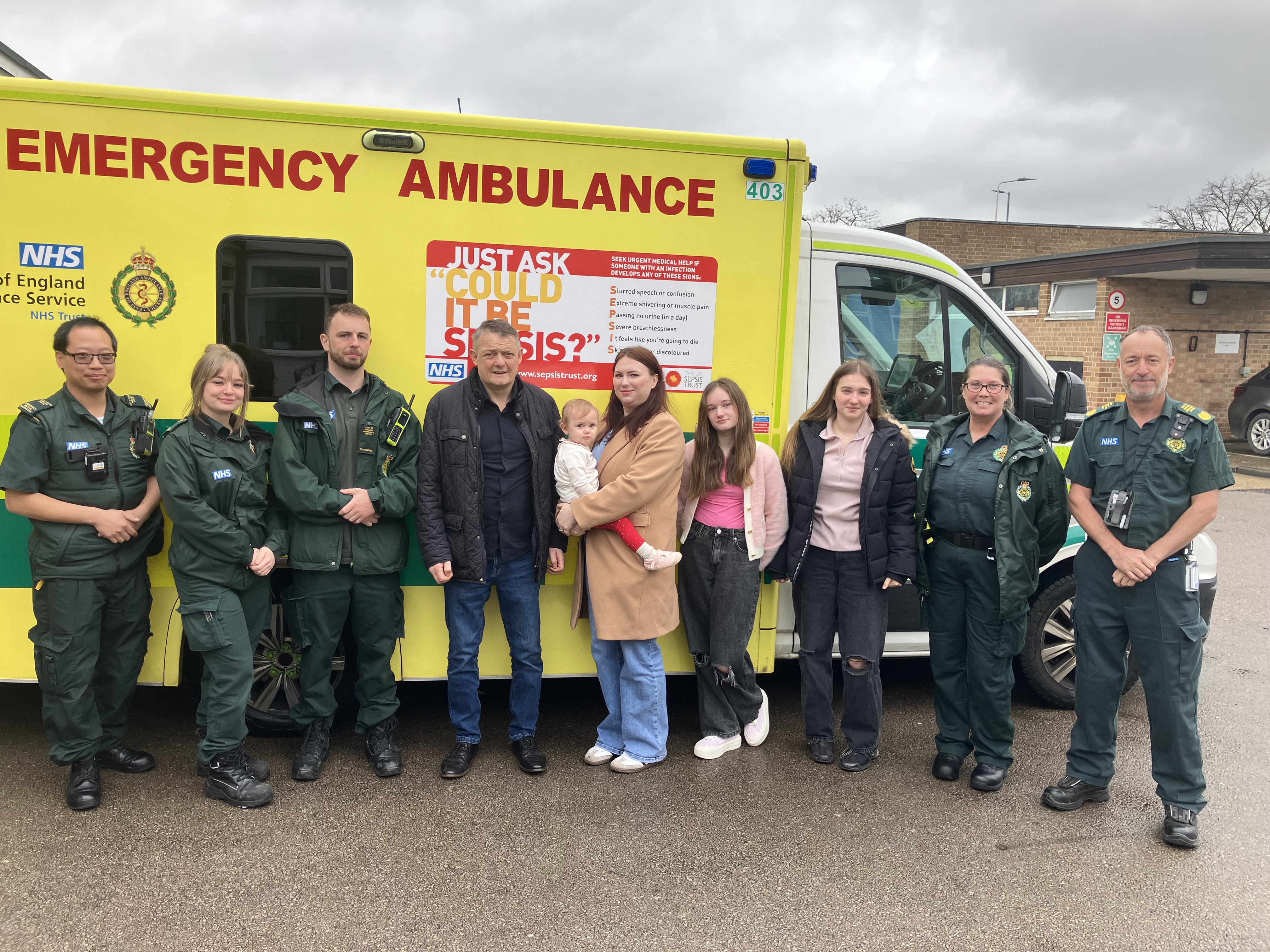 Ken Christy stands with partner Gemma, daughter Grace, Gemma’s daughters Katie and Erin, and Clinical Operations lead Mike Bates in front of an ambulance during a visit to thank the crew who saved his life.