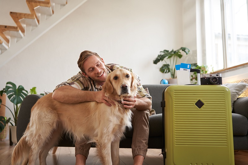 Hombre abrazando a su perro Golden Retriever junto a una maleta preparada para un viaje de Semana Santa