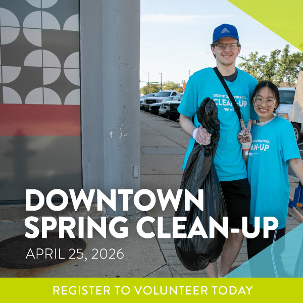 Two people wearing blue "Downtown Wichita Clean-Up" T-shirts stand on a sidewalk holding a large garbage bag. Text on the image reads: "Downtown Spring Clean-Up, April 25, 2026. Register to Volunteer Today.”