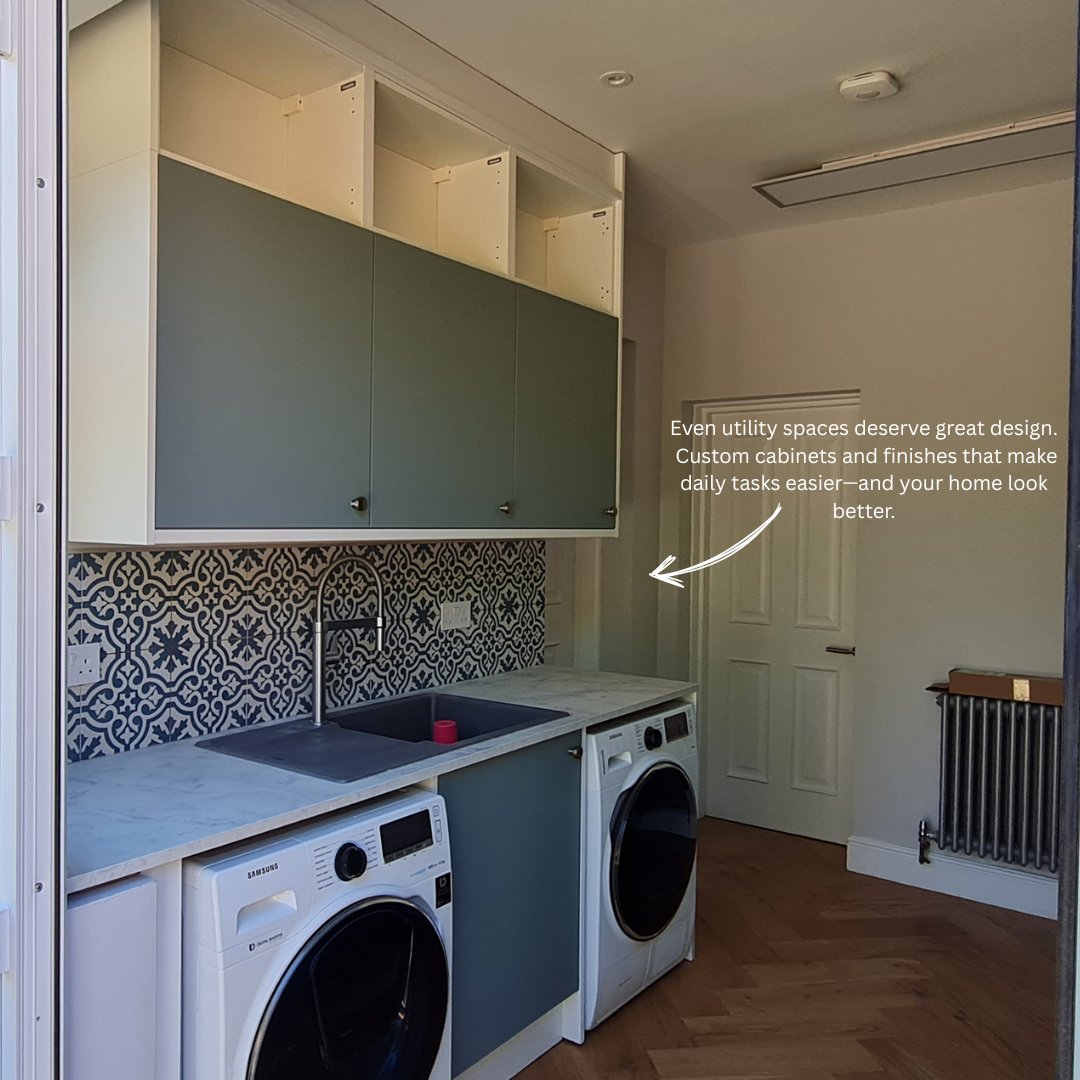 A modern utility room featuring sage green custom cabinetry. A white marble-effect countertop holds a dark grey sink with a tall chrome faucet. Below the counter are two white Samsung washing machines with a matching green cabinet door between them. The backsplash is a blue and white Moroccan-style pattern. Open shelving units are visible above the closed green cabinets.