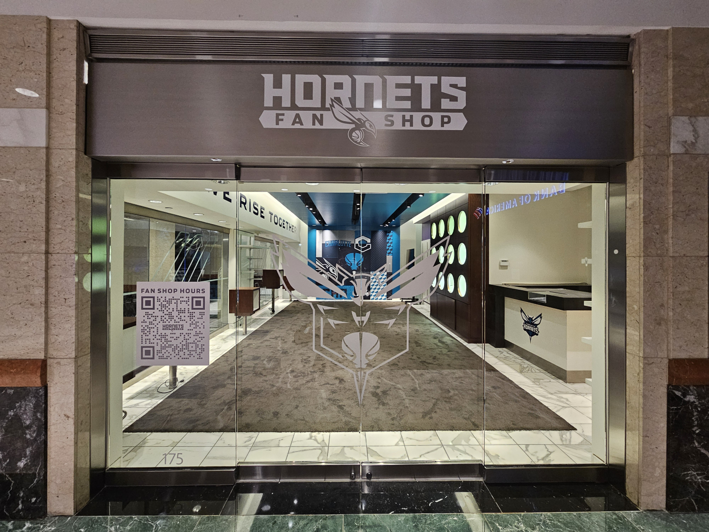 Hornets Fan Shop storefront with glass doors featuring team hornet logo and QR code sign displaying fan shop hours.