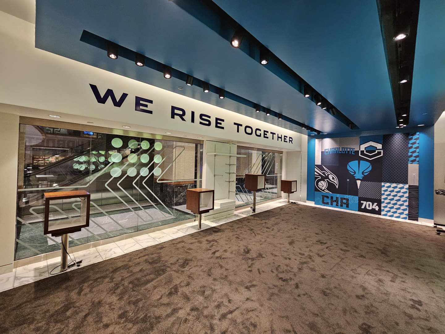 Lobby with 'WE RISE TOGETHER' slogan, blue ceiling, glass display cases and Charlotte-themed blue mural.